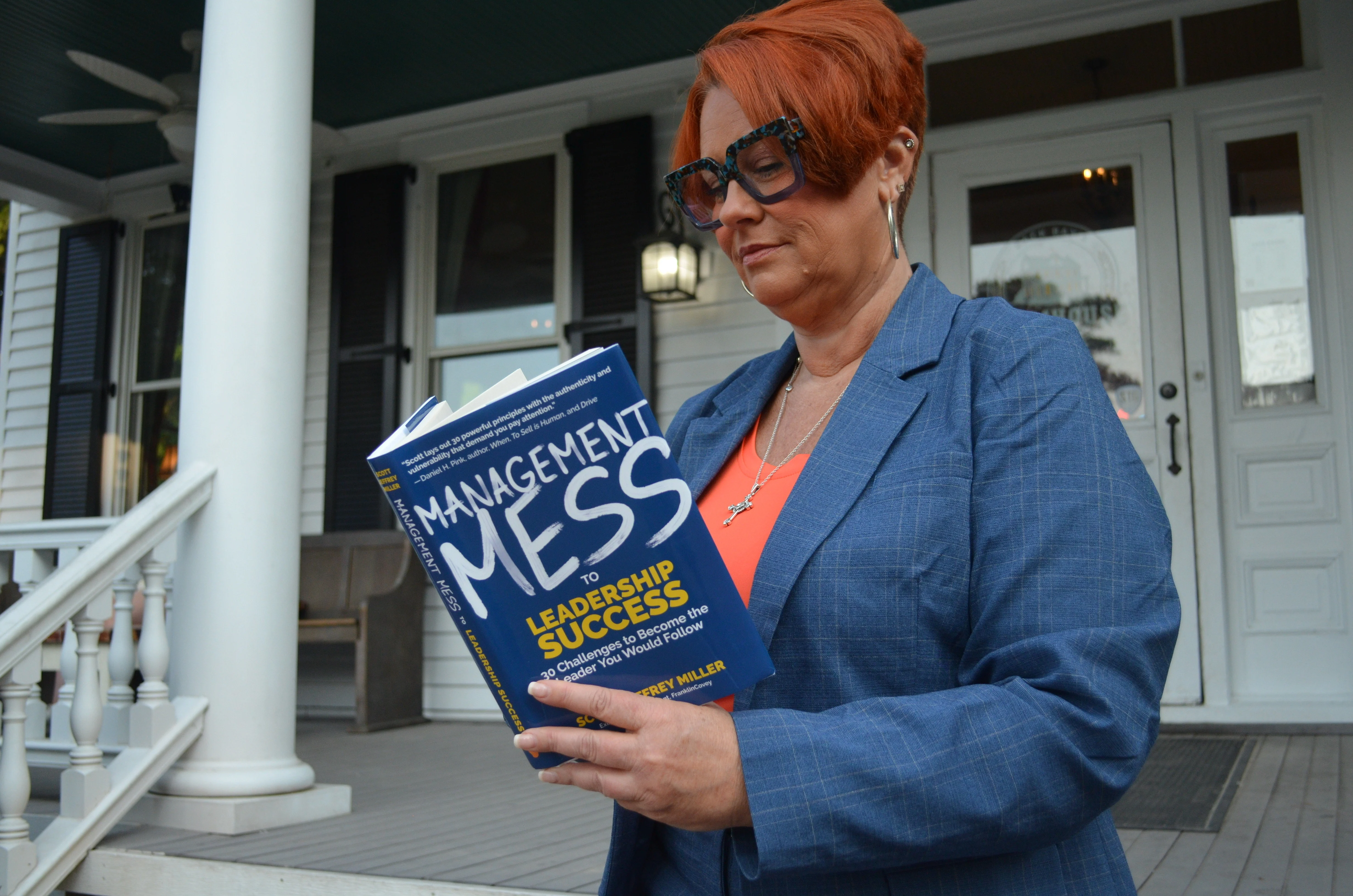 Corrina Carter on a porch, reading a copy of Management Mess to Leadership Success
